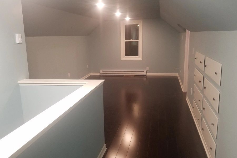 Empty loft with dark wood floors, gray walls, built-in drawers, and a small window.