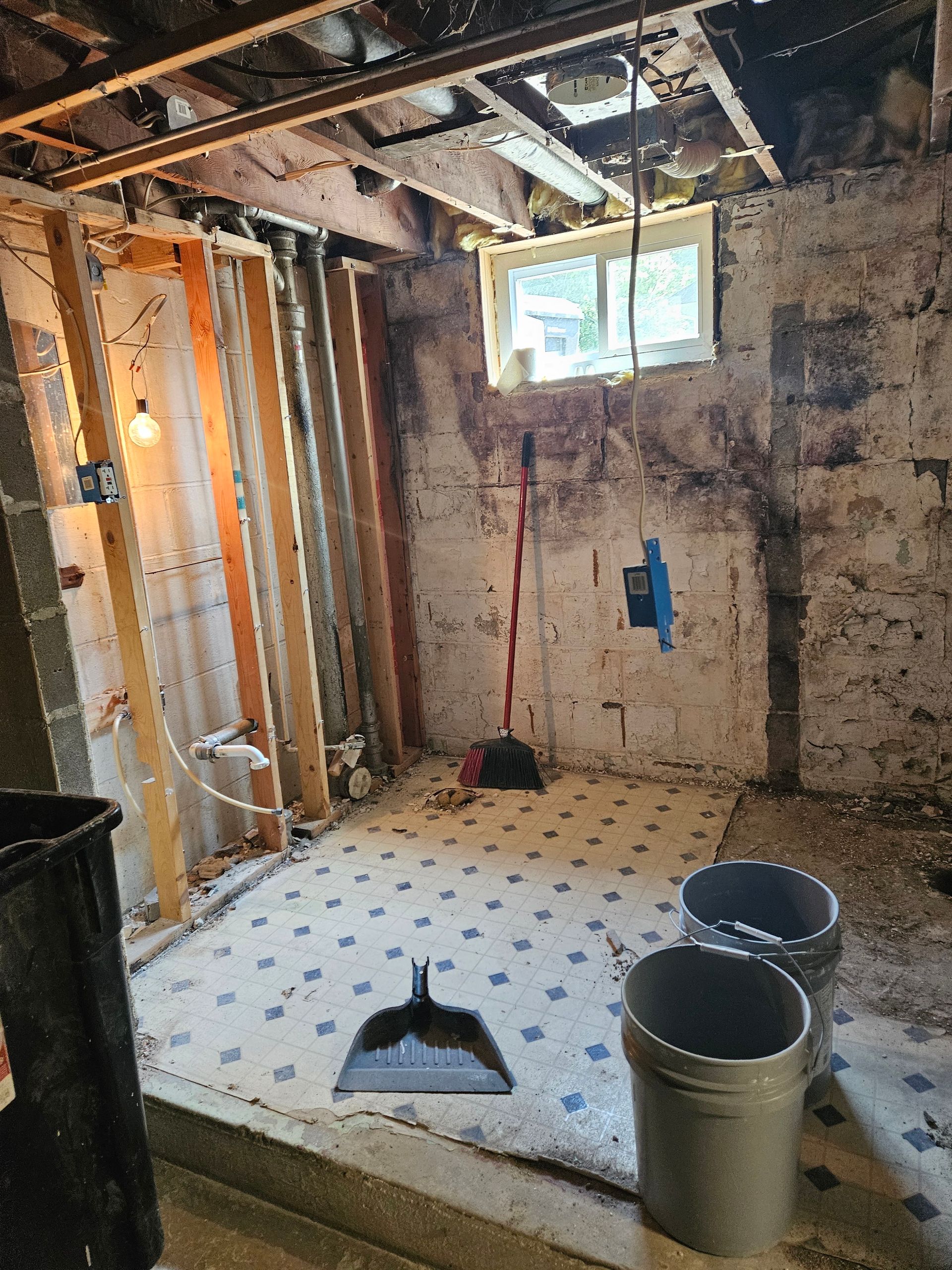 Partially stripped bathroom under renovation with exposed studs, debris, and tools on the floor
