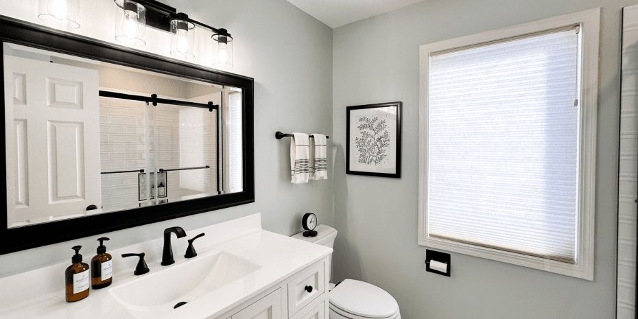 Modern bathroom with black-framed mirror, white vanity, and window blinds