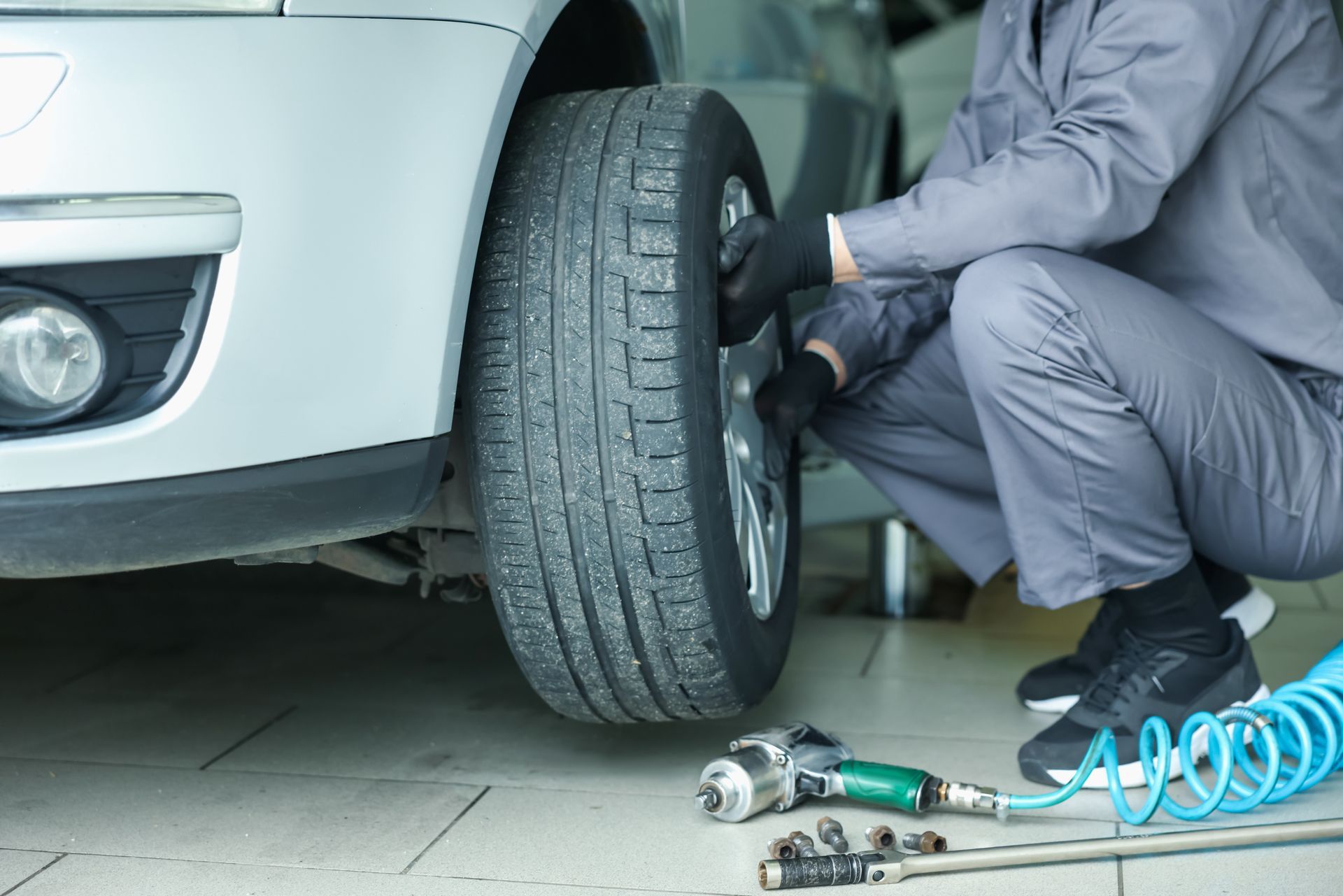 A car mechanic changing a car wheel and tire with tools scattered around him.