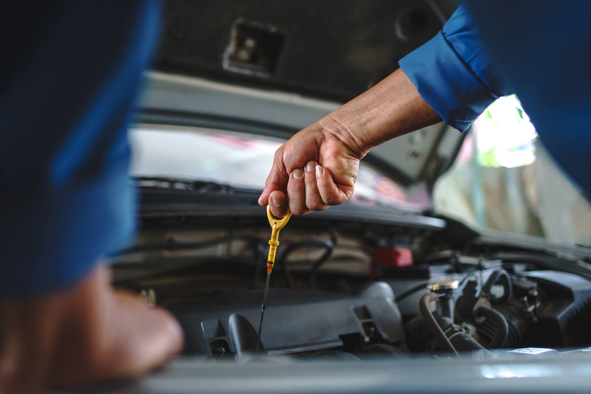 An auto mechanic is checking the engine oil in a vehicle at a garage.