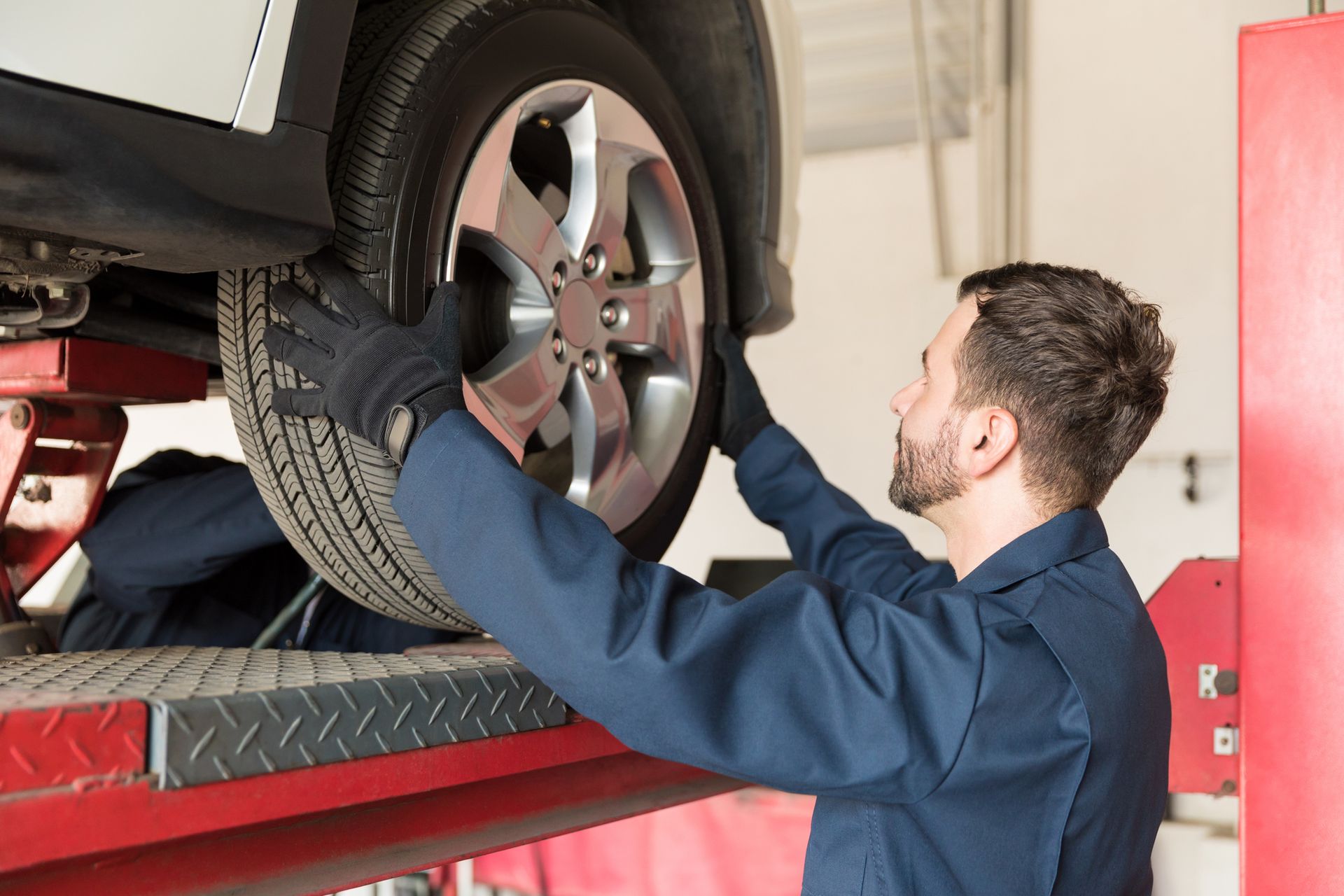 A tire change provider is inspecting tire alignment on a lifted vehicle at an auto shop.