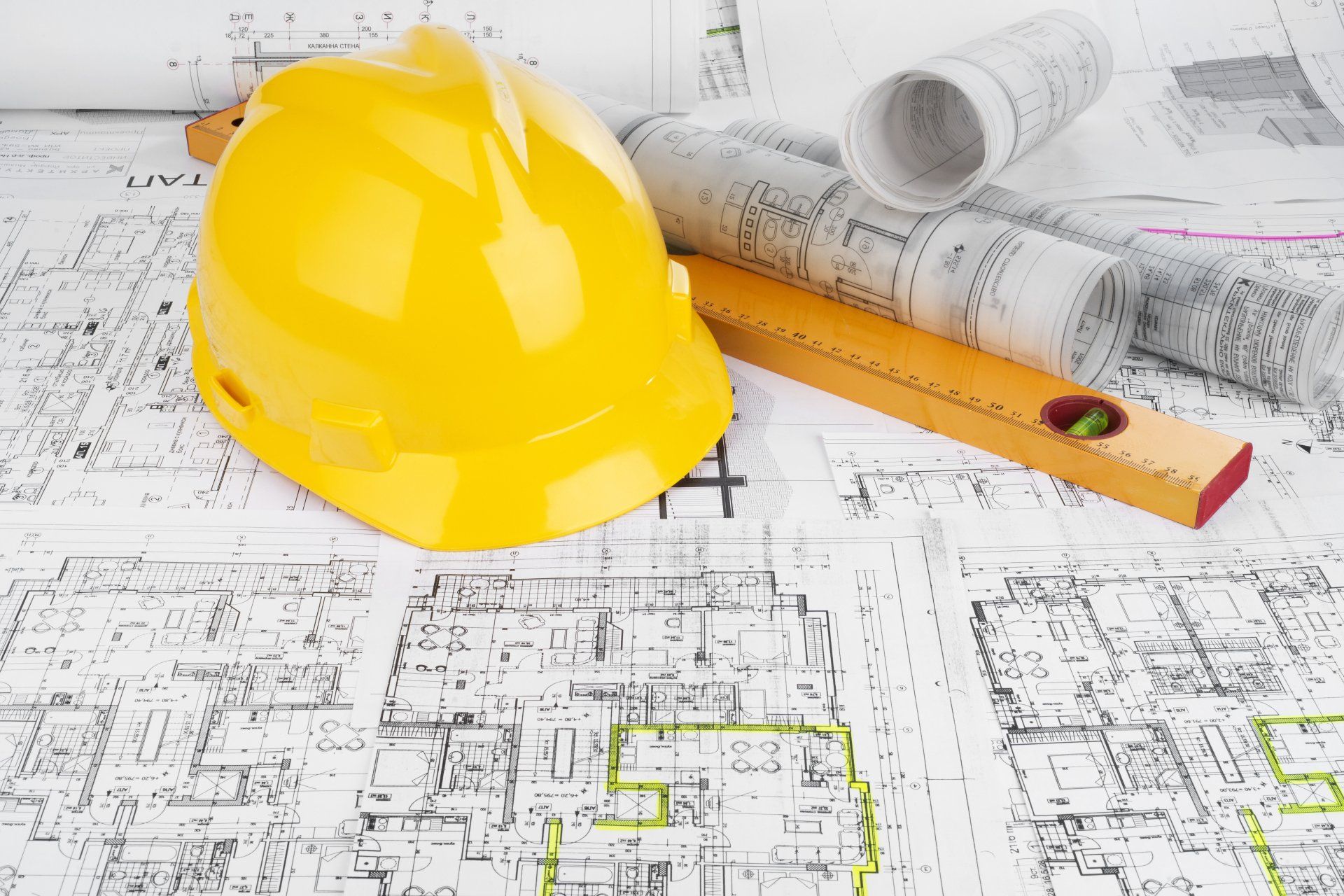 Yellow hard hat and level rest on architectural blueprints.