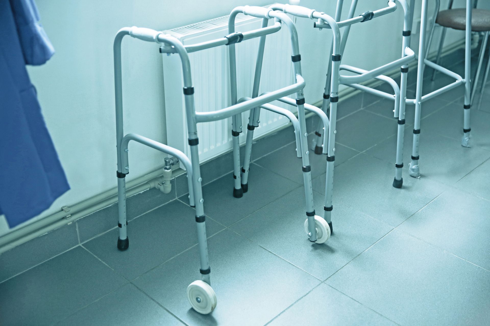 Caminantes blancos alineados en el suelo de baldosas azules de un hospital cerca de una cortina.