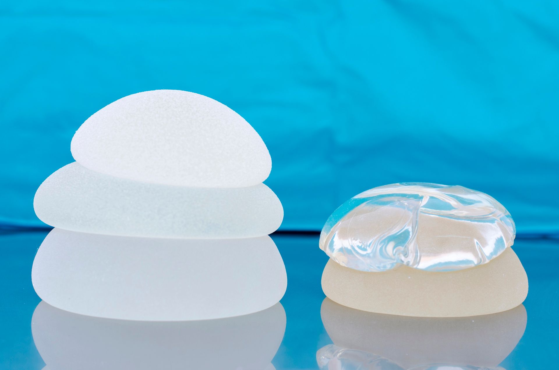 Dos copas menstruales de silicona blanca sobre un fondo azul, una de ellas con tapa transparente.
