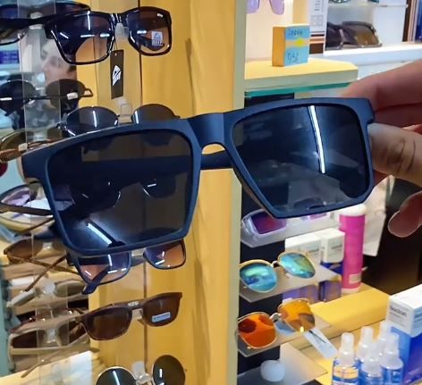 Unas gafas de sol grandes y oscuras se exhiben en un estante de una tienda junto con otras gafas y accesorios.