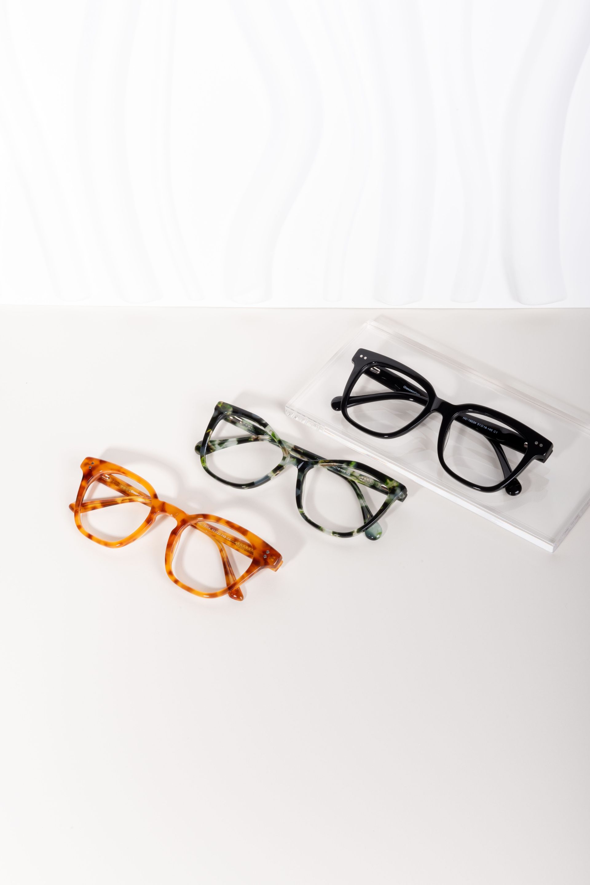 Tres monturas de gafas en naranja, transparente y negro sobre una superficie blanca.