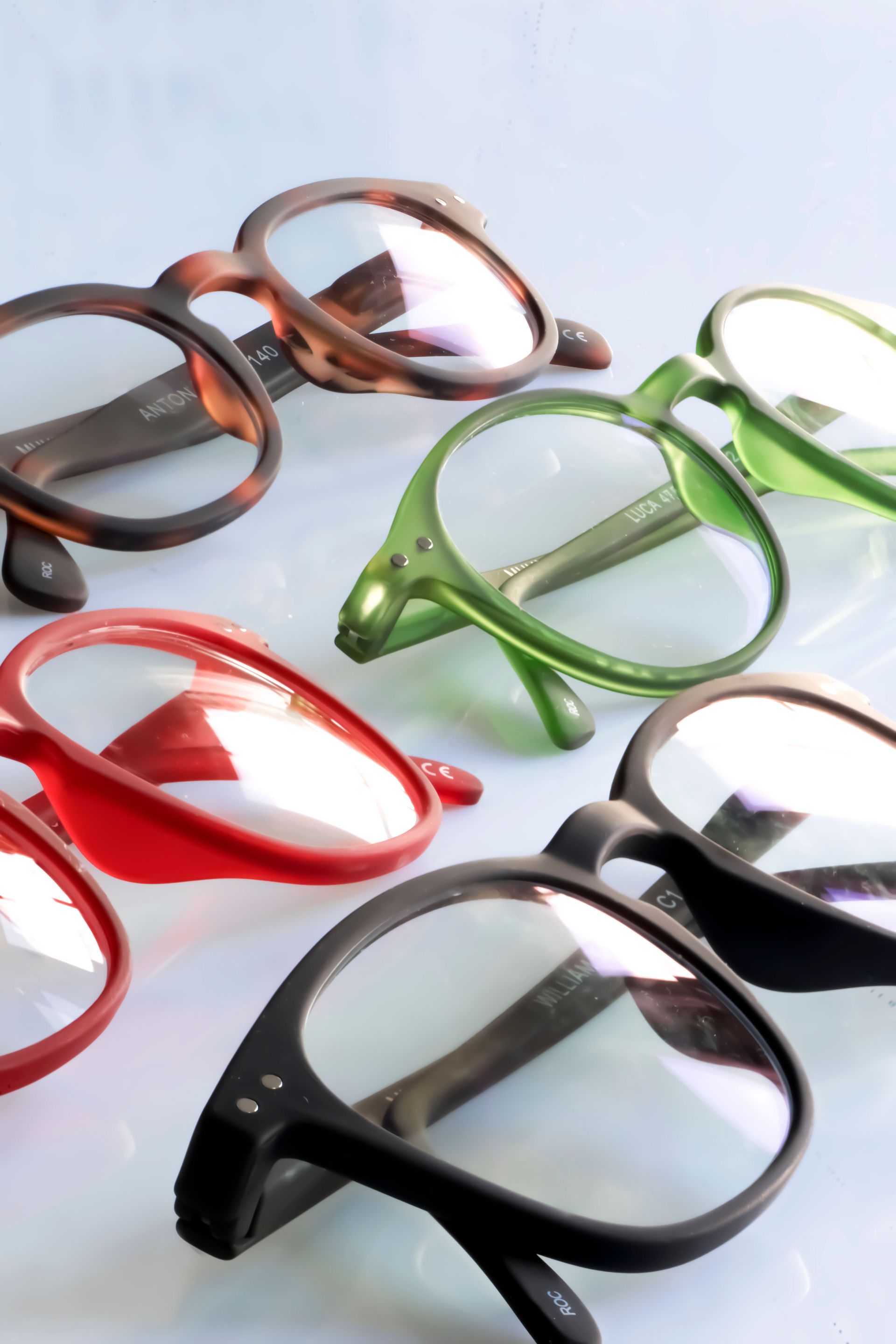 Monturas de gafas coloridas en rojo, verde, marrón, negro y gris sobre un fondo blanco.