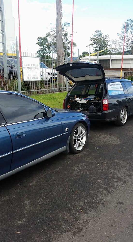 A Blue Car is Parked Next to a Black Car With the Trunk Open — South Coast Locksmiths in Helensburgh, NSW