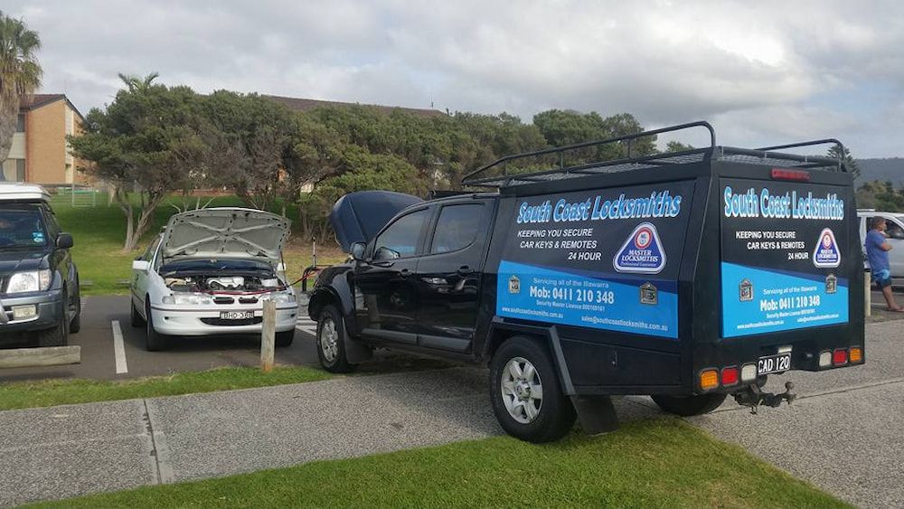 A Black Truck With a Trailer Attached to It is Parked Next to a White Car — South Coast Locksmiths in Bulli, NSW