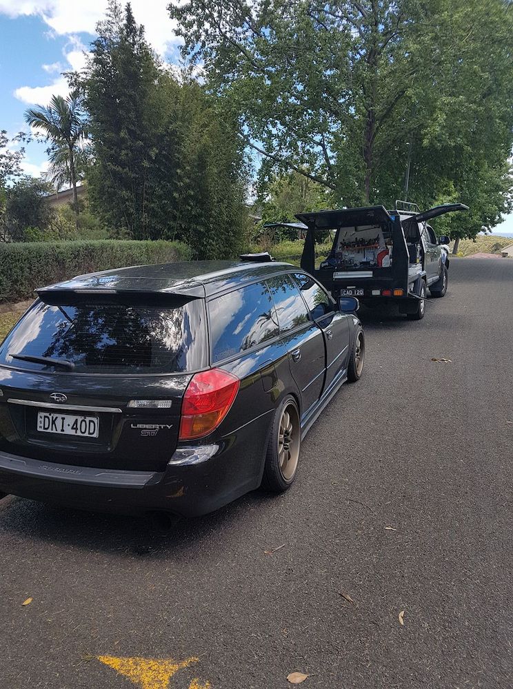 A Black Car is Parked on the Side of the Road Next to a Tow Truck — South Coast Locksmiths in Kiama, NSW
