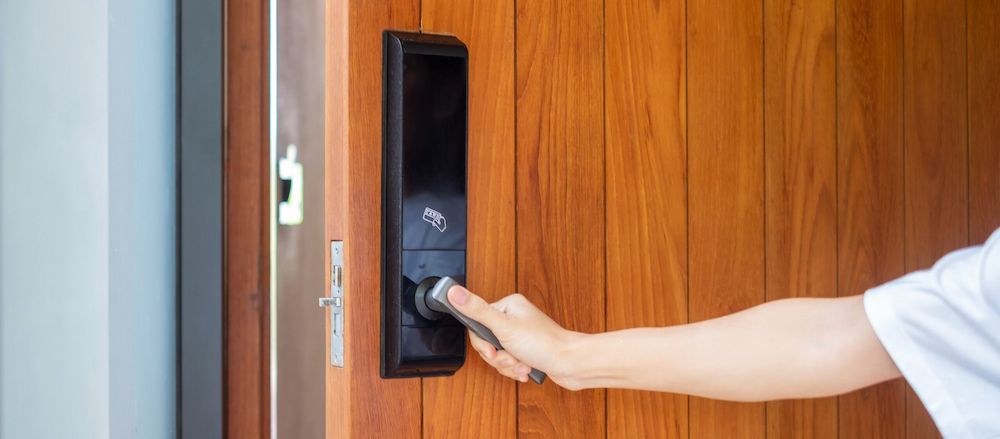 A Person is Using a Smart Door Lock to Open a Wooden Door — South Coast Locksmiths in Austinmer, NSW