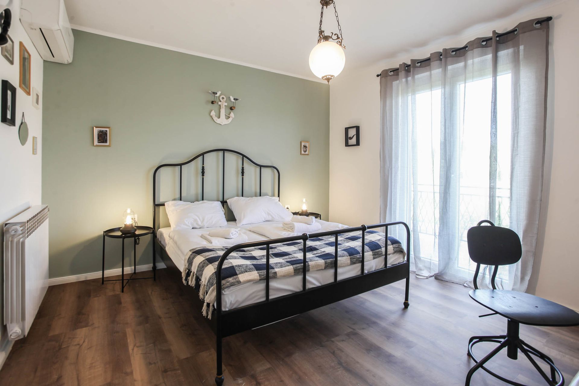 Bright bedroom with black metal bed, white bedding, wood floor, and sheer curtains by a window