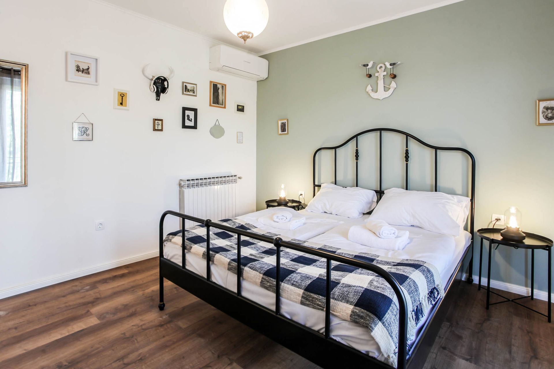 Bright bedroom with black metal bed, white bedding, pale green walls, and wooden floor.