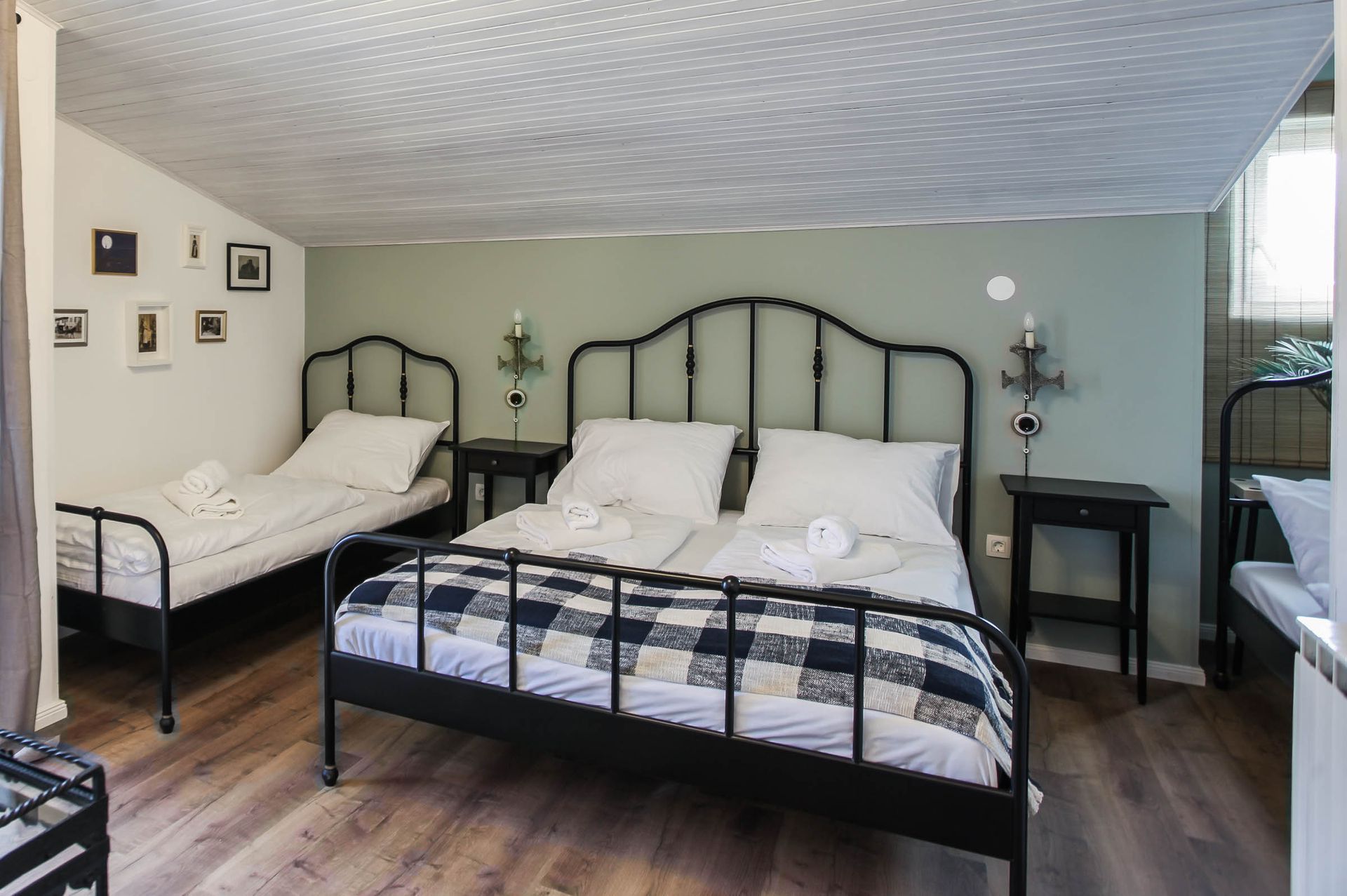 Bedroom with two black metal beds, white bedding, wood floors, and a small side table.