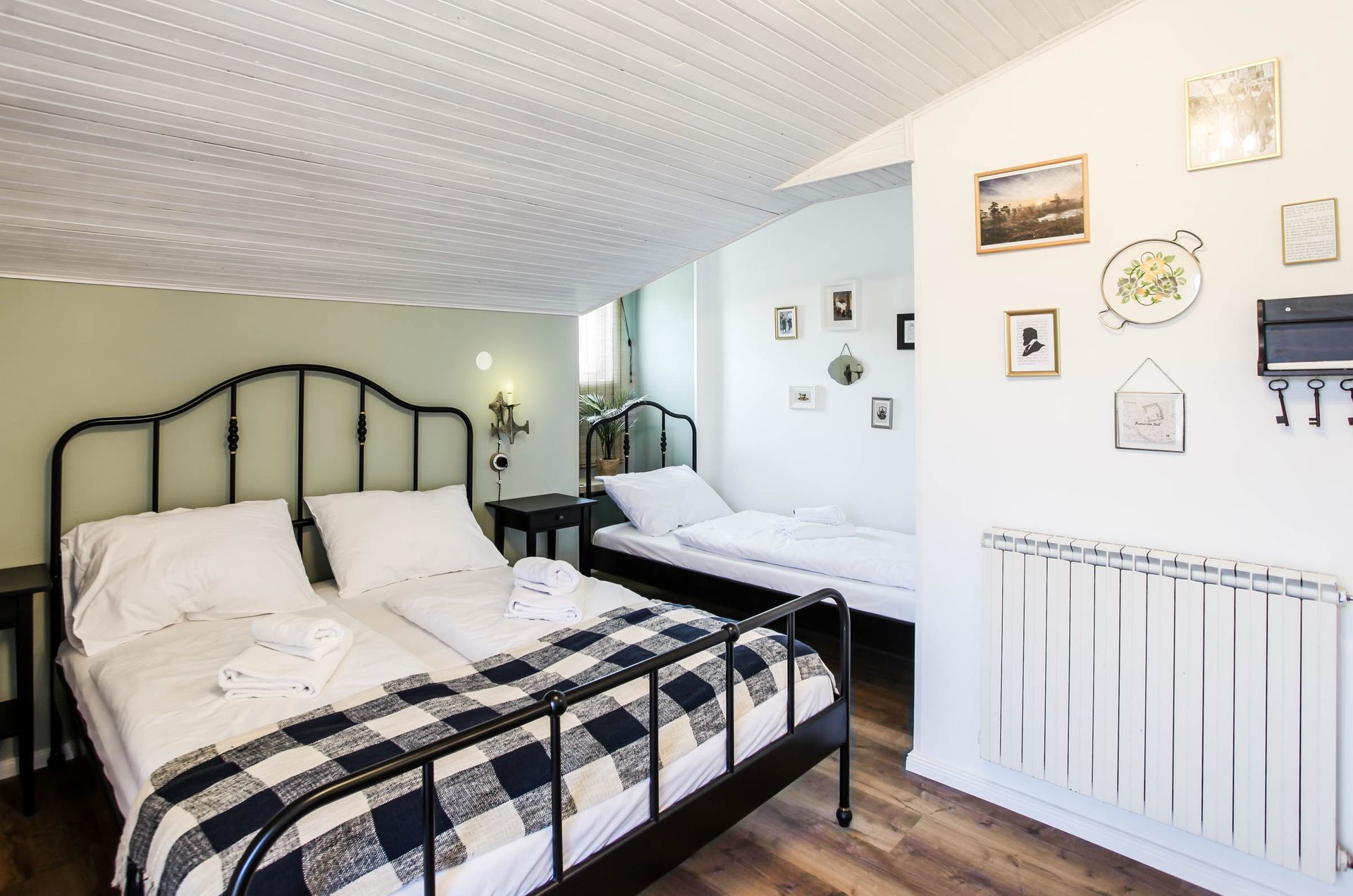 Bright bedroom with black iron bed, plaid bedding, mirrored dresser, and white walls with wall art