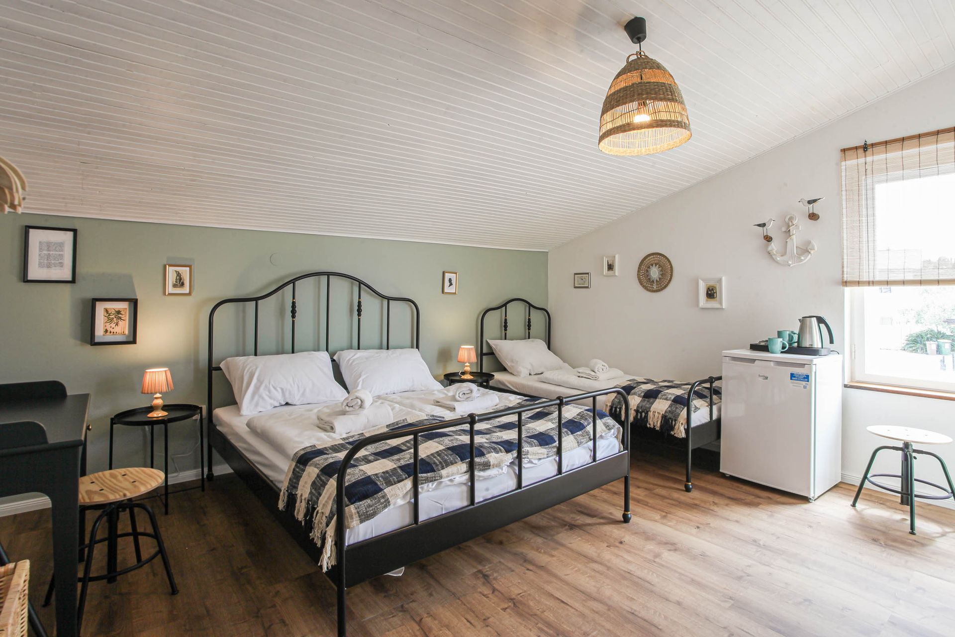 Cozy bedroom with black-and-white bed, wooden floors, soft green walls, and a bright window nook