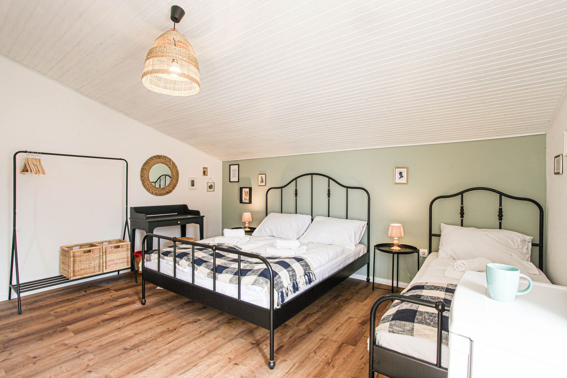 Bright bedroom with two black metal beds, white bedding, wood floor, and soft green walls