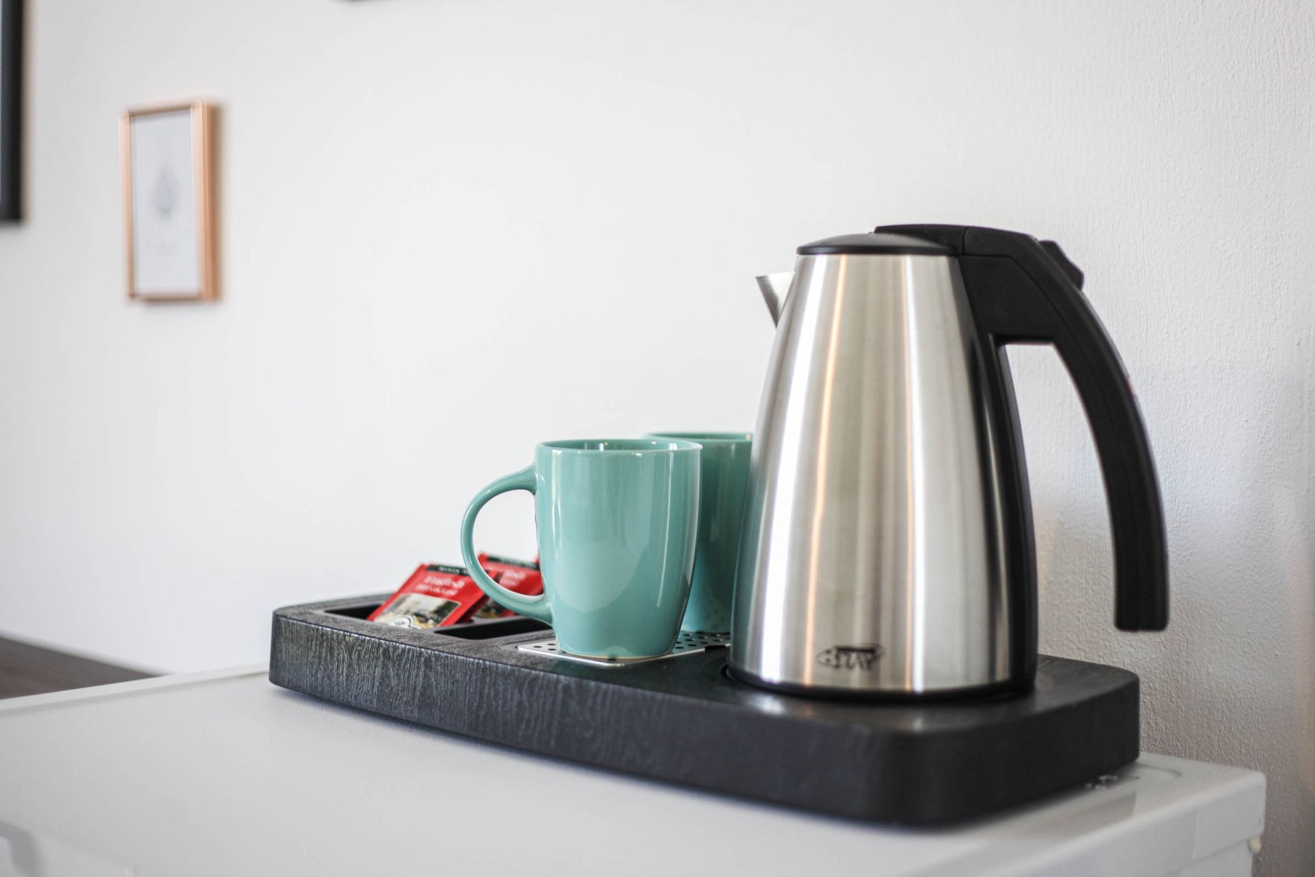 Stainless steel kettle and teal mug on a tray on a countertop