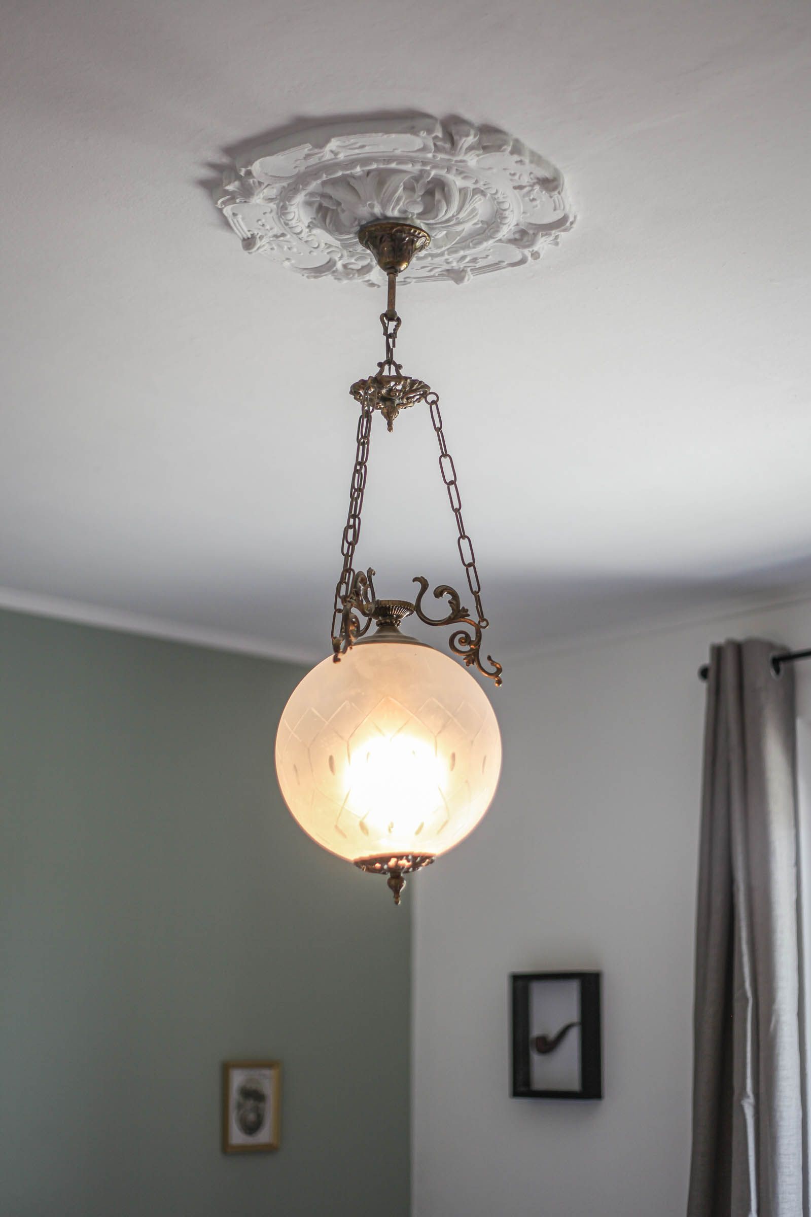 Vintage hanging globe chandelier with chain, lit in a room with a decorative ceiling medallion.