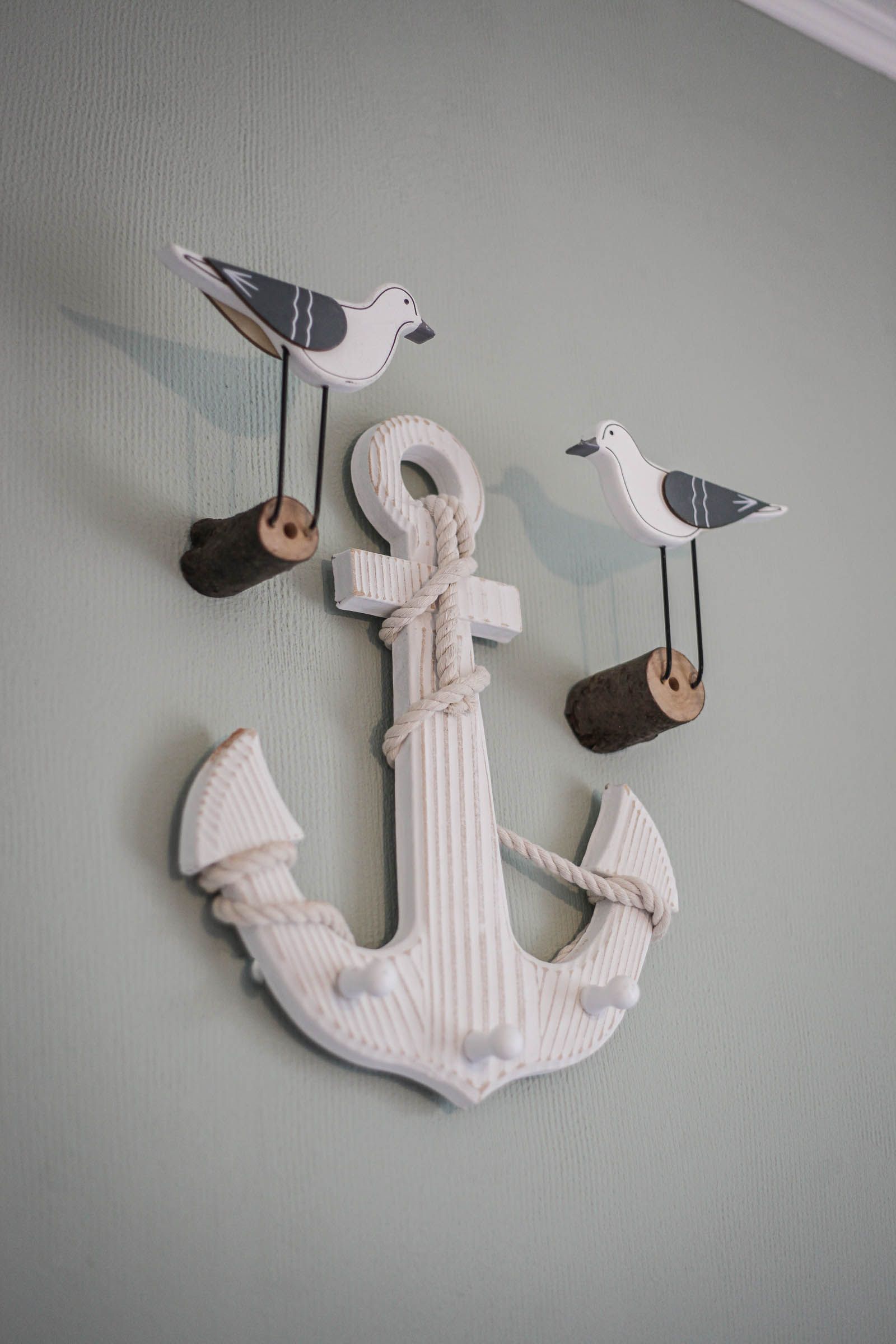 White decorative anchor wall hanging with two bird ornaments on a pale green wall.