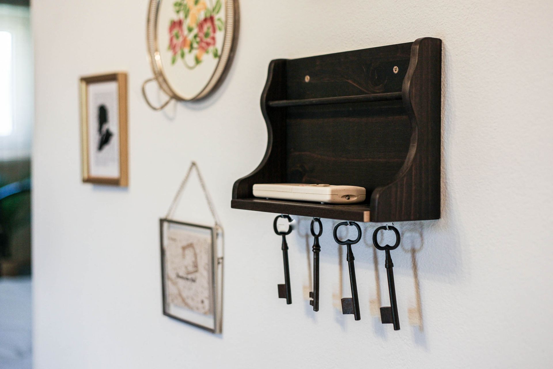 Black key rack with four keys hanging on a white wall beside framed art.