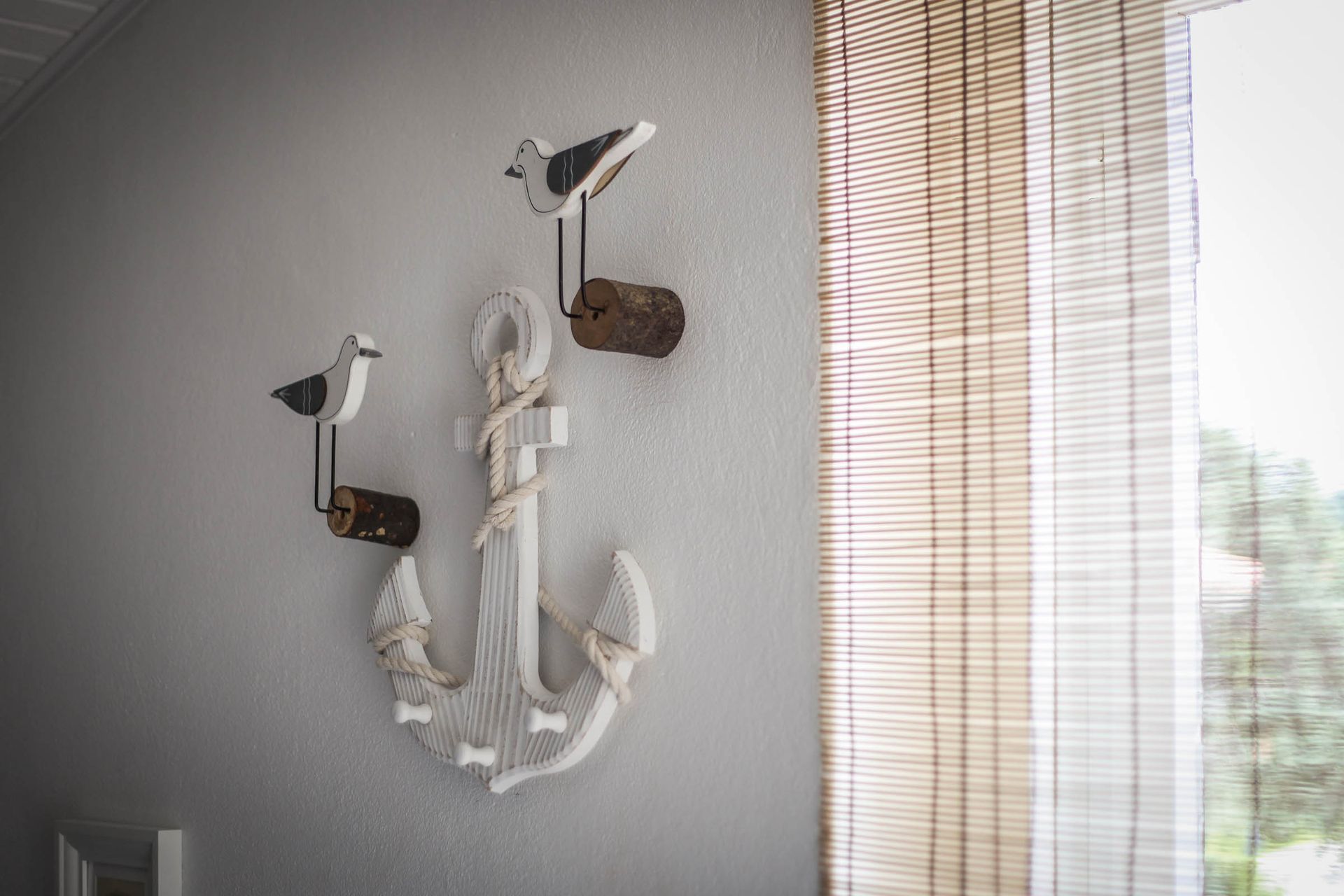 Wall-mounted nautical bird sculpture in white and brown on a gray wall beside a window blind