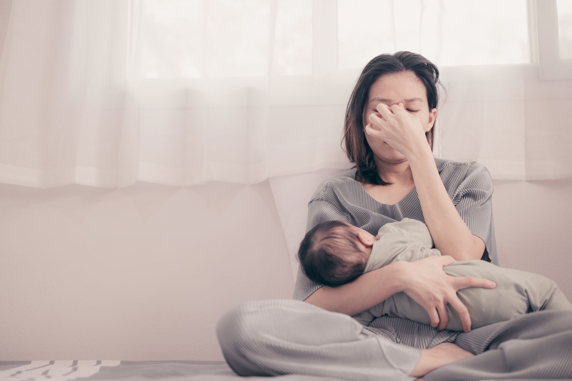 Woman sitting on the floor, holding a child and covering her face, looking distressed Woman sitting on the floor, holding a child and covering her face, looking distressed