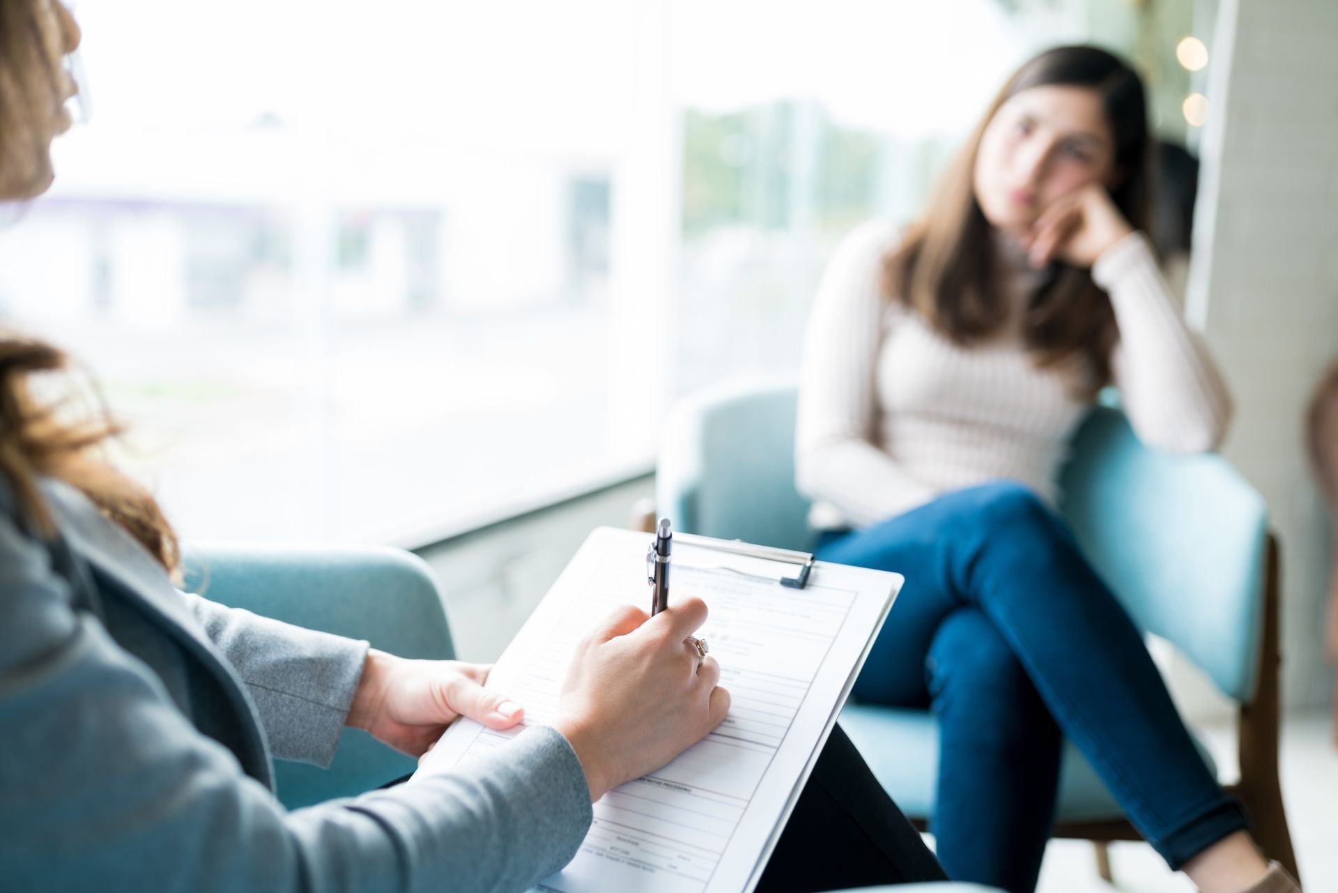 Therapist taking notes while speaking with a seated client in a bright office Therapist taking notes while speaking with a seated client in a bright office