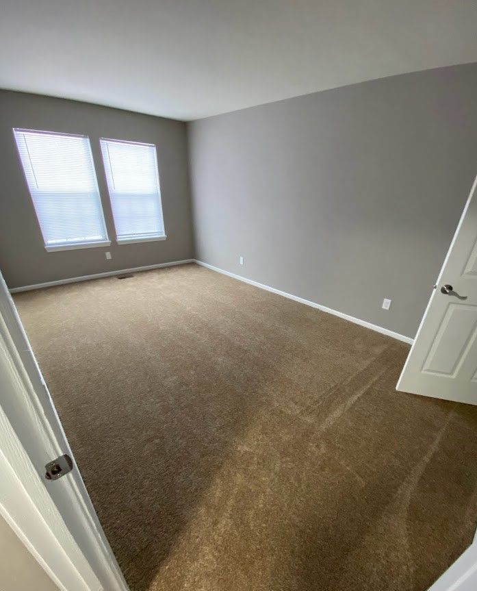 An empty bedroom with a brown carpet and two windows.