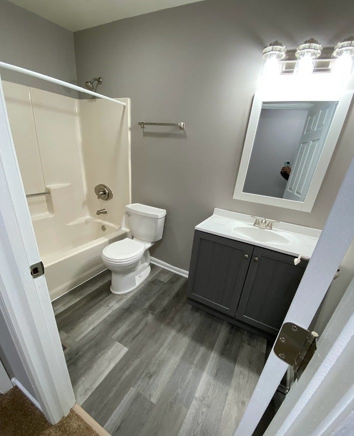 A bathroom with a toilet , sink , bathtub and mirror.