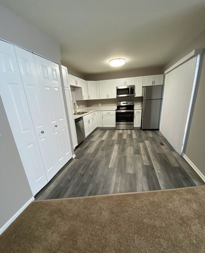A kitchen with white cabinets , stainless steel appliances , a refrigerator and a microwave.