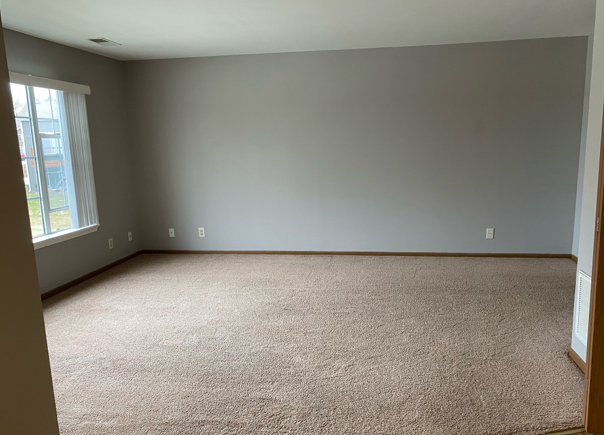 An empty living room with a large carpeted floor and a window.