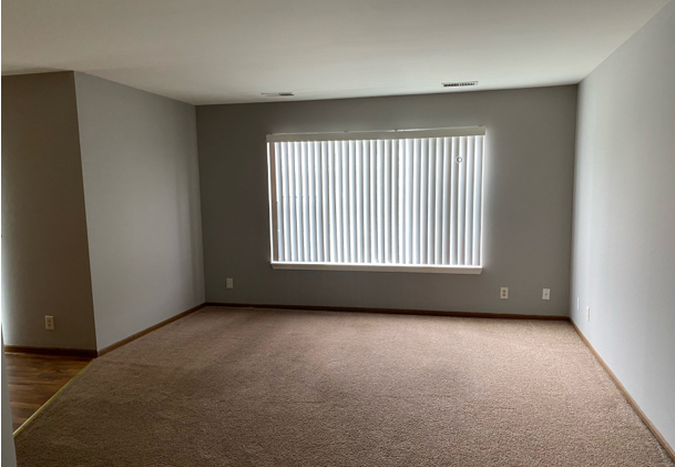 An empty living room with a large window and blinds.