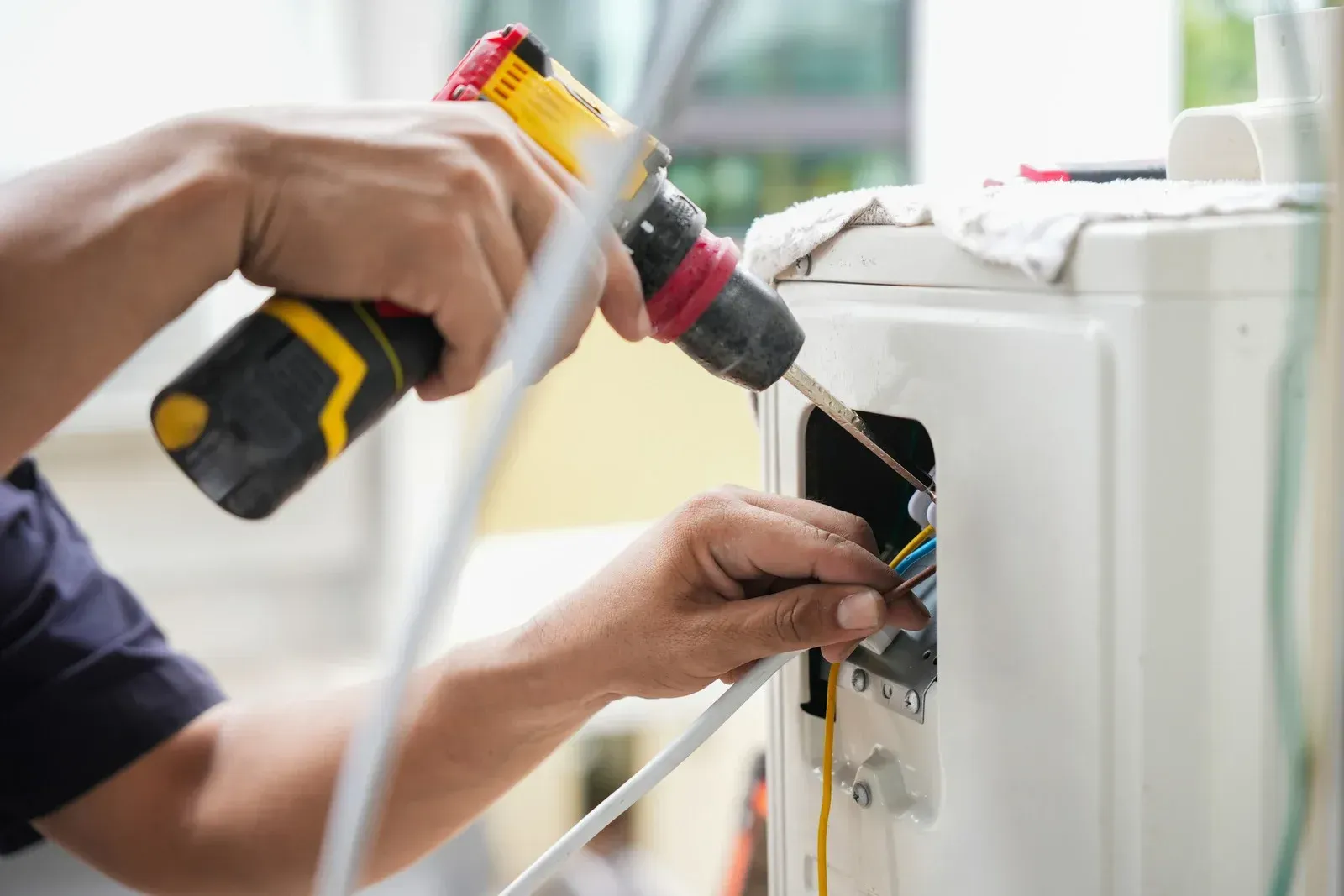 Electrician uses a drill to work on wiring inside of a white appliance.