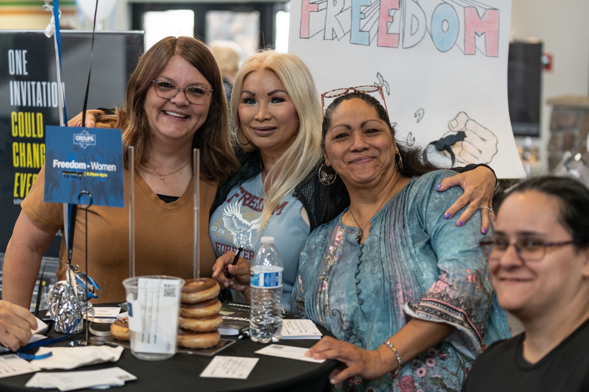 Four people smiling at a table with pamphlets and signs at a community event booth