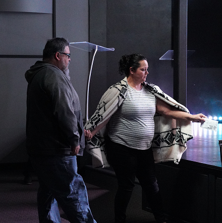 Two people viewing a glowing exhibit in a dark gallery, one reaching toward the display