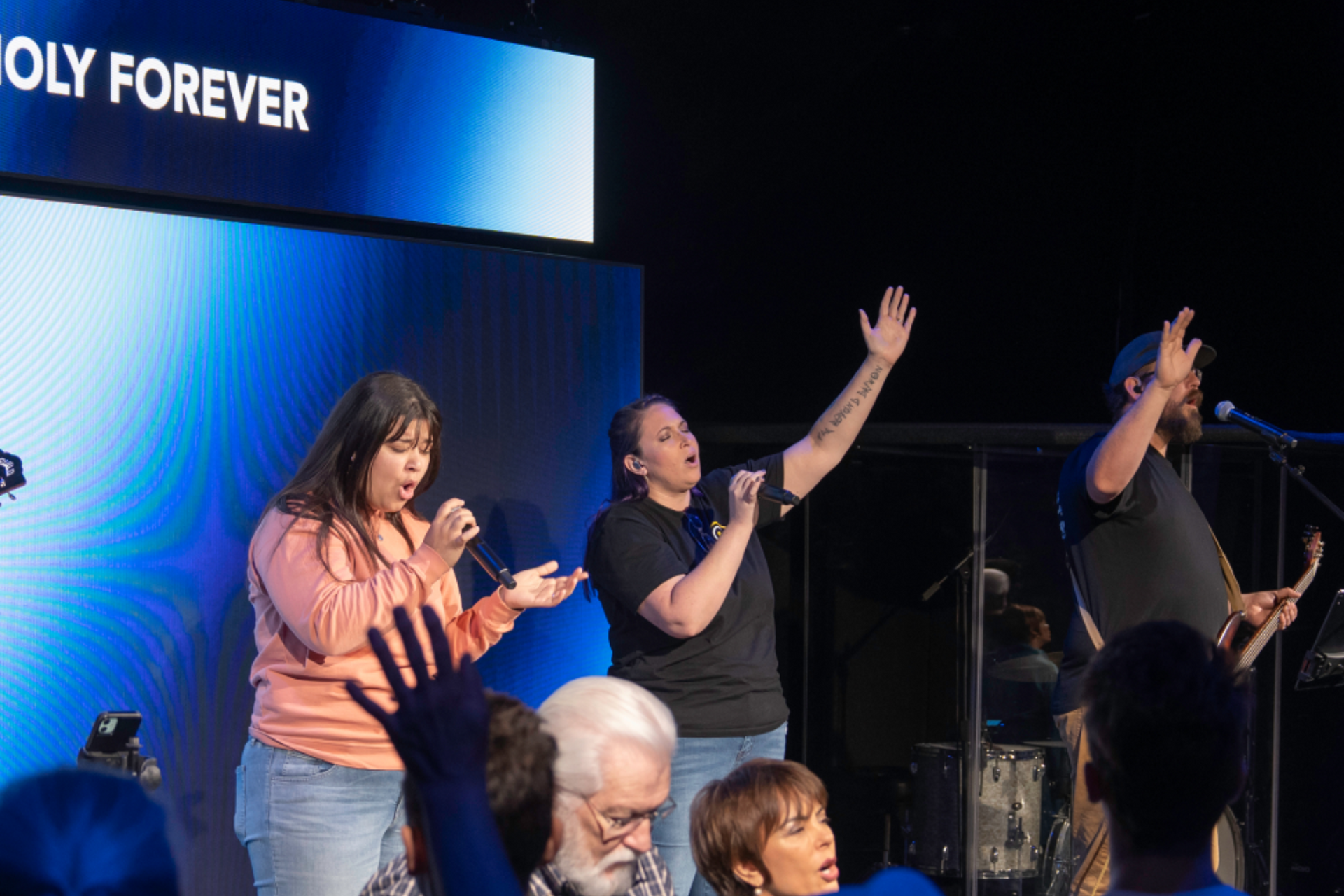 Worship team singing on stage with raised hands under blue lights at a church service