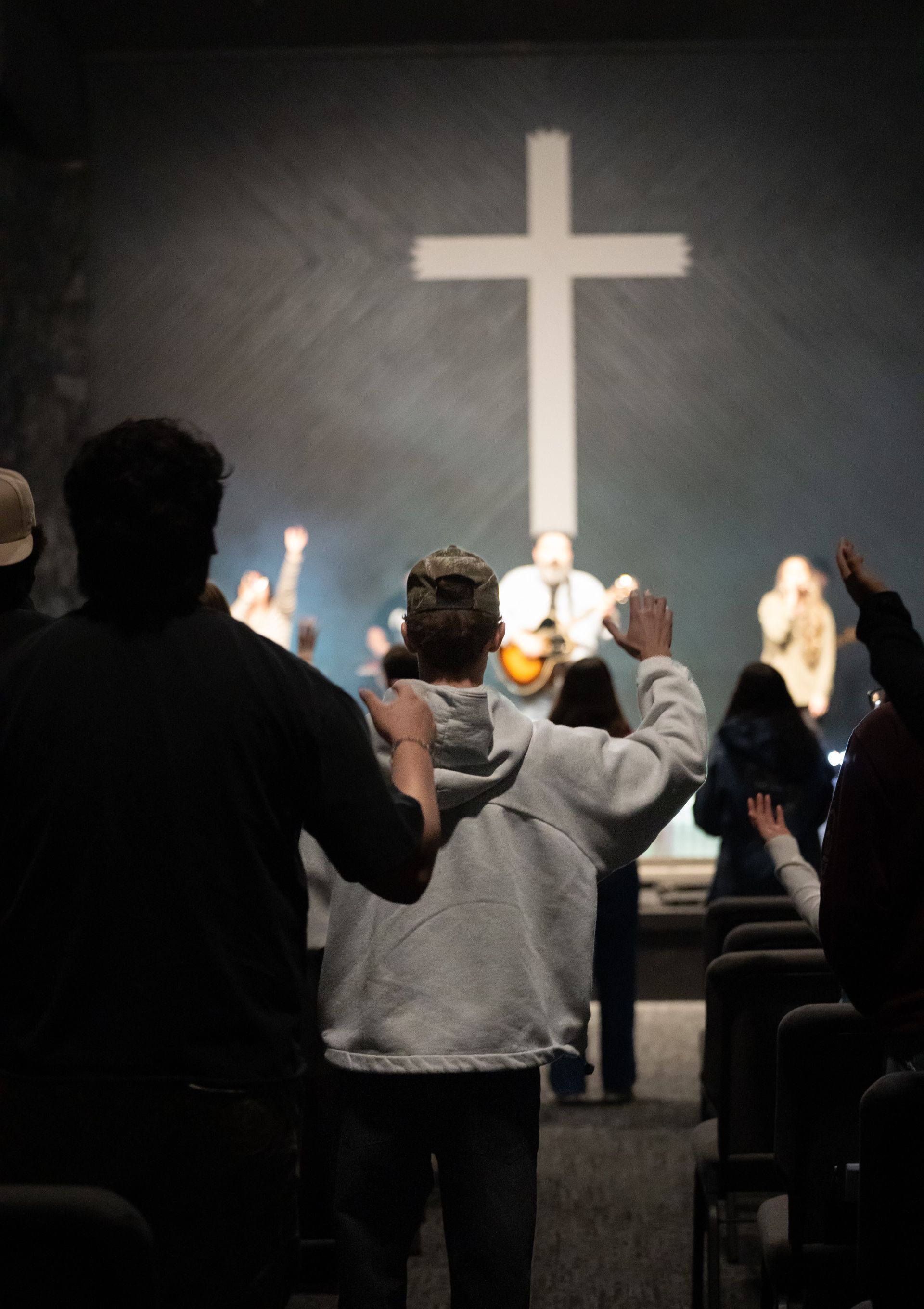 People worshiping in a dim church before a large illuminated cross