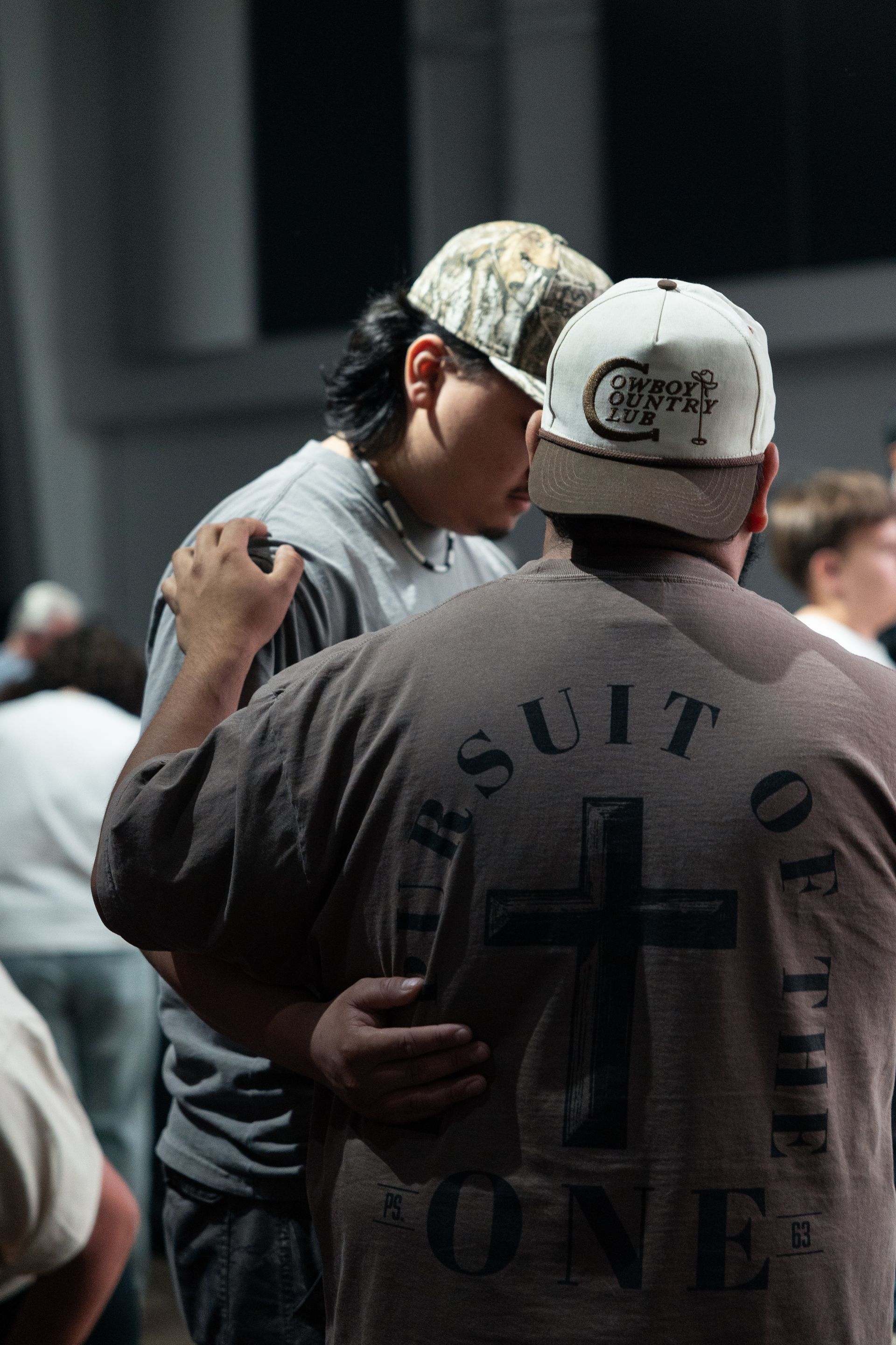 Two people embracing at a concert, one in a white cap and black shirt with “Suits on” printed on the back.