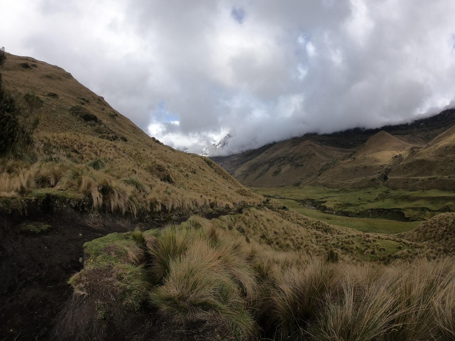 Cloudy mountain valley with grassy hills and a dark stream in the foreground