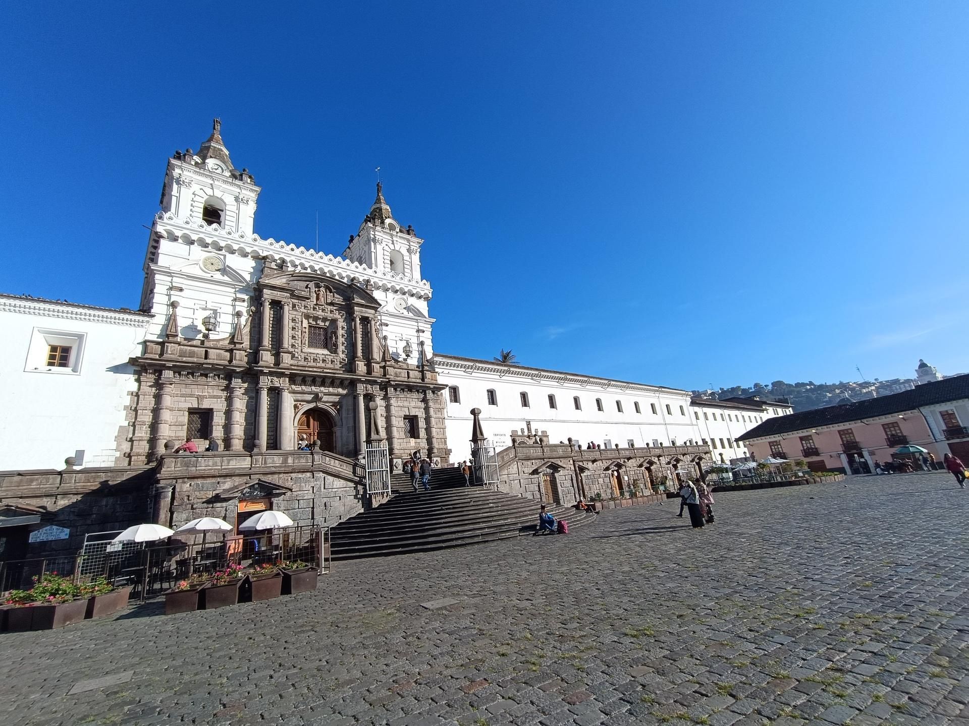Historic cathedral on a cobblestone plaza under a bright blue sky, with outdoor café seating nearby