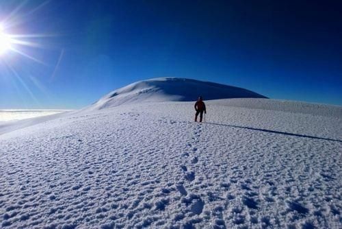 Person standing on snowy hill under bright sun and blue sky