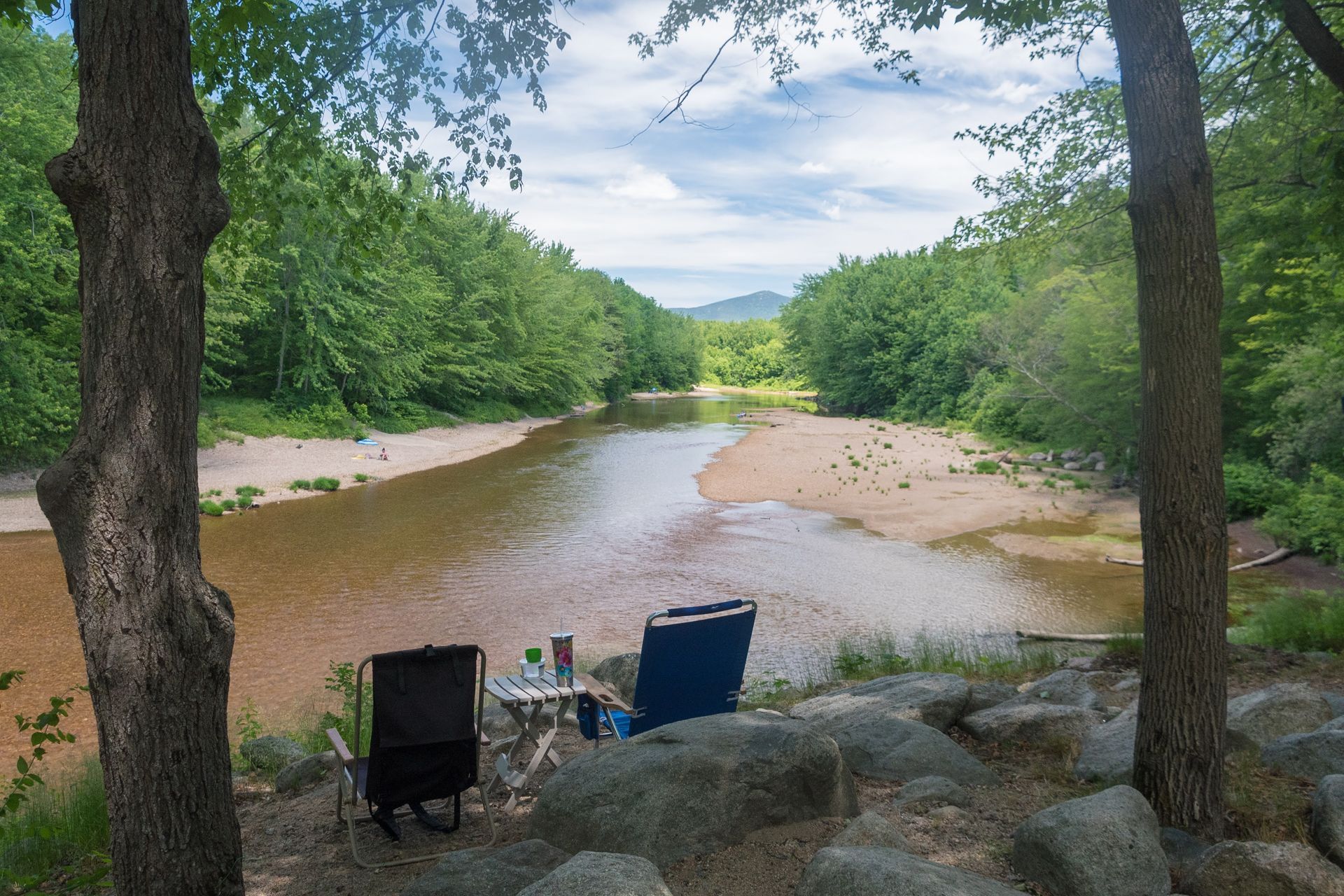 Two chairs are sitting on a rock near a river.