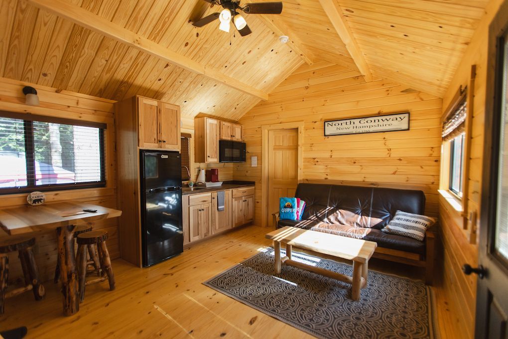 A living room in a log cabin with a couch , table , and refrigerator.