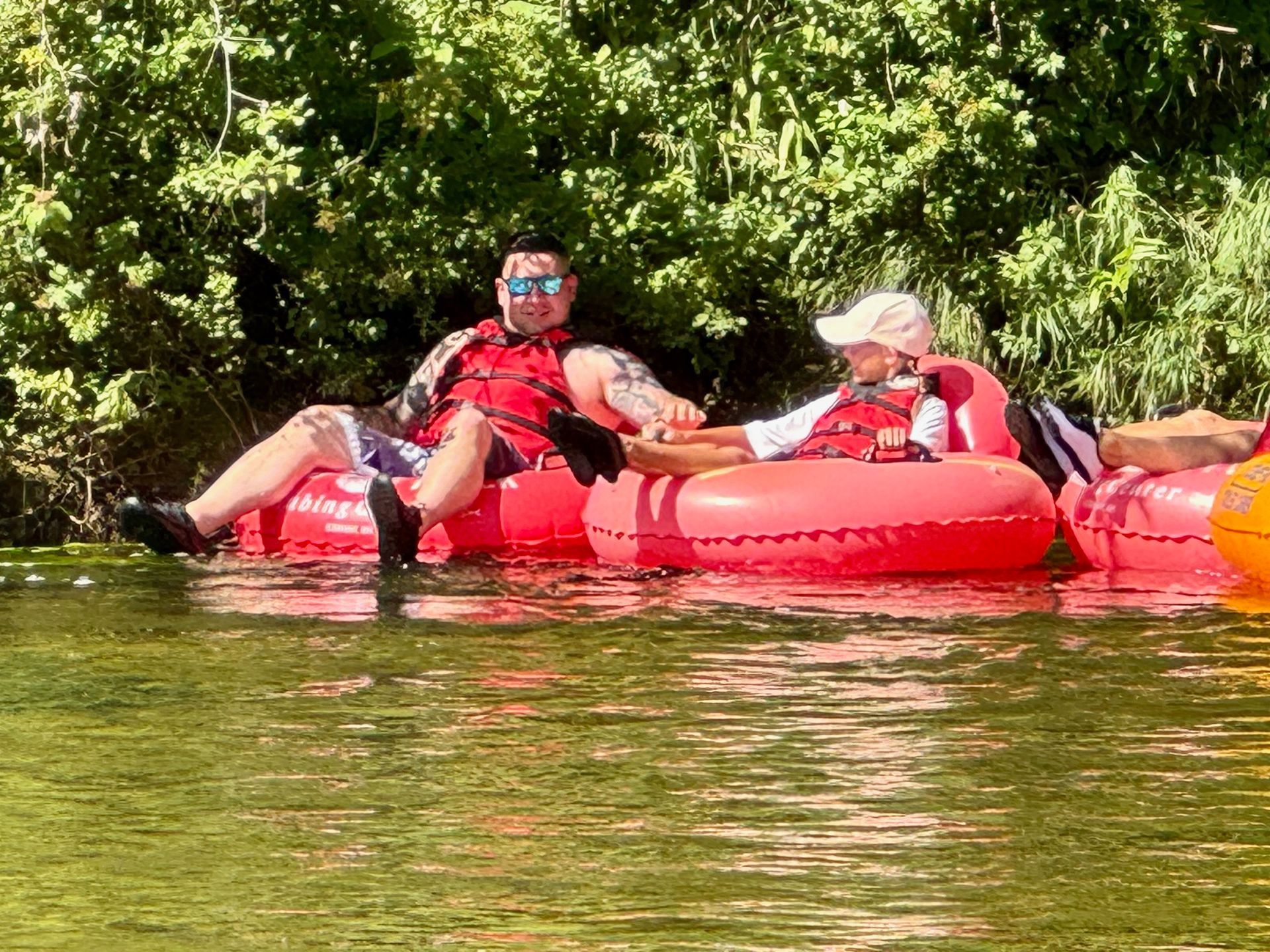 People floating on a red raft in calm water near dense green trees