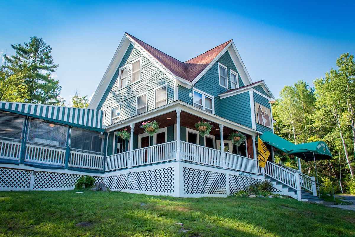 A large green house with a red roof and a large porch surrounded by trees.
