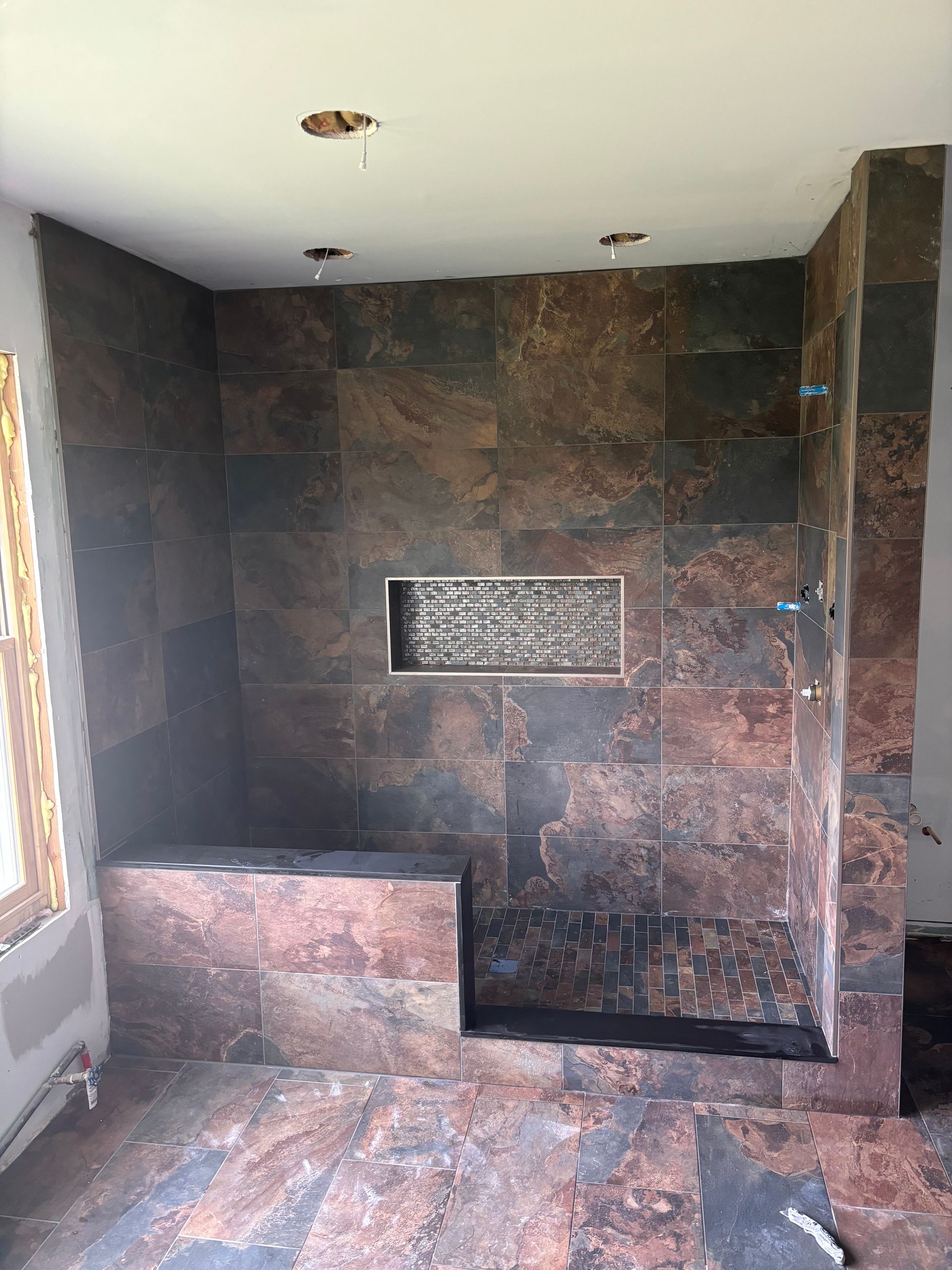 Shower with dark brown tile, built-in bench, and recessed shelf.