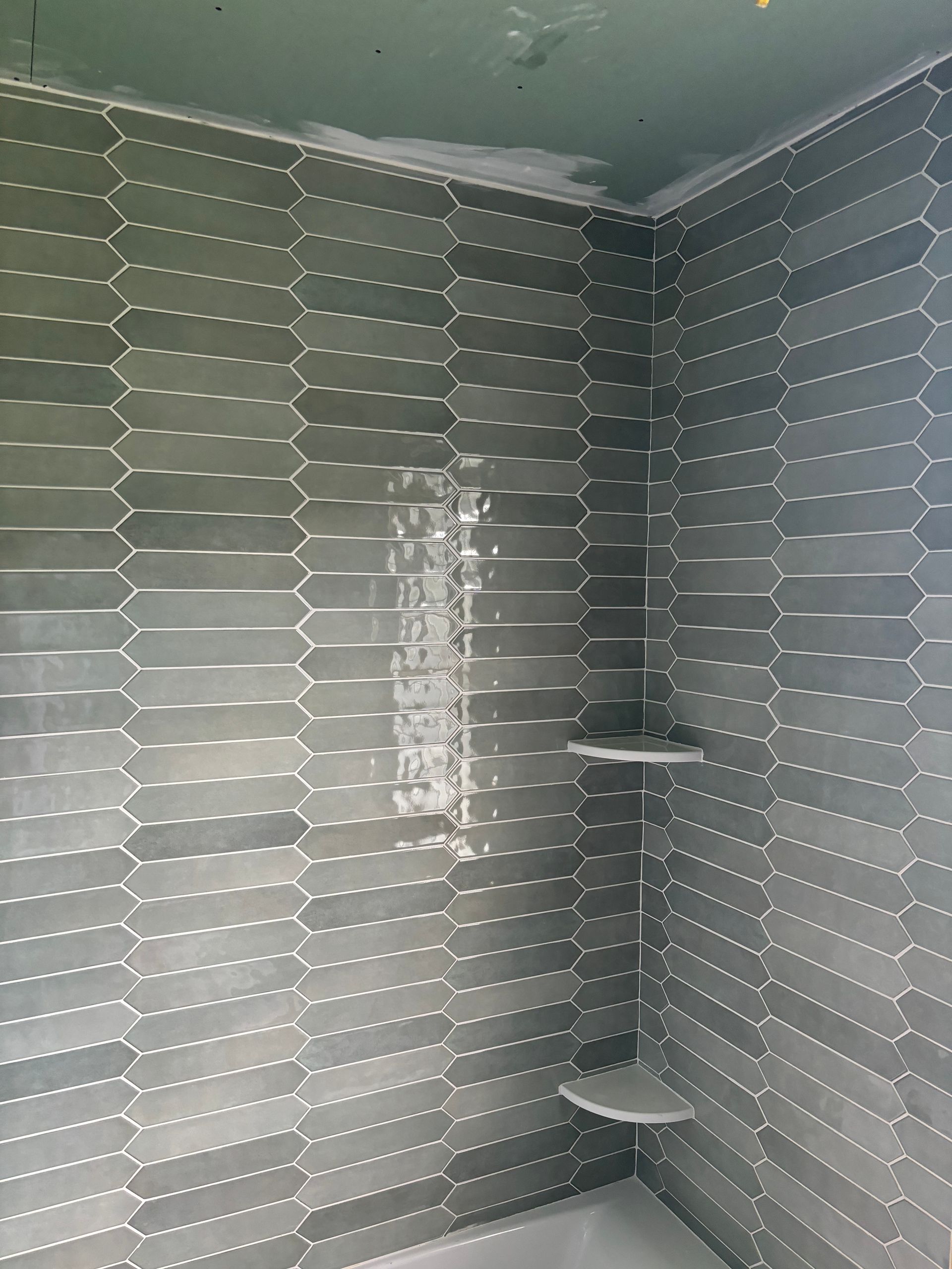 Gray tile shower with built-in shelf, walls partially tiled. Green drywall at the top.