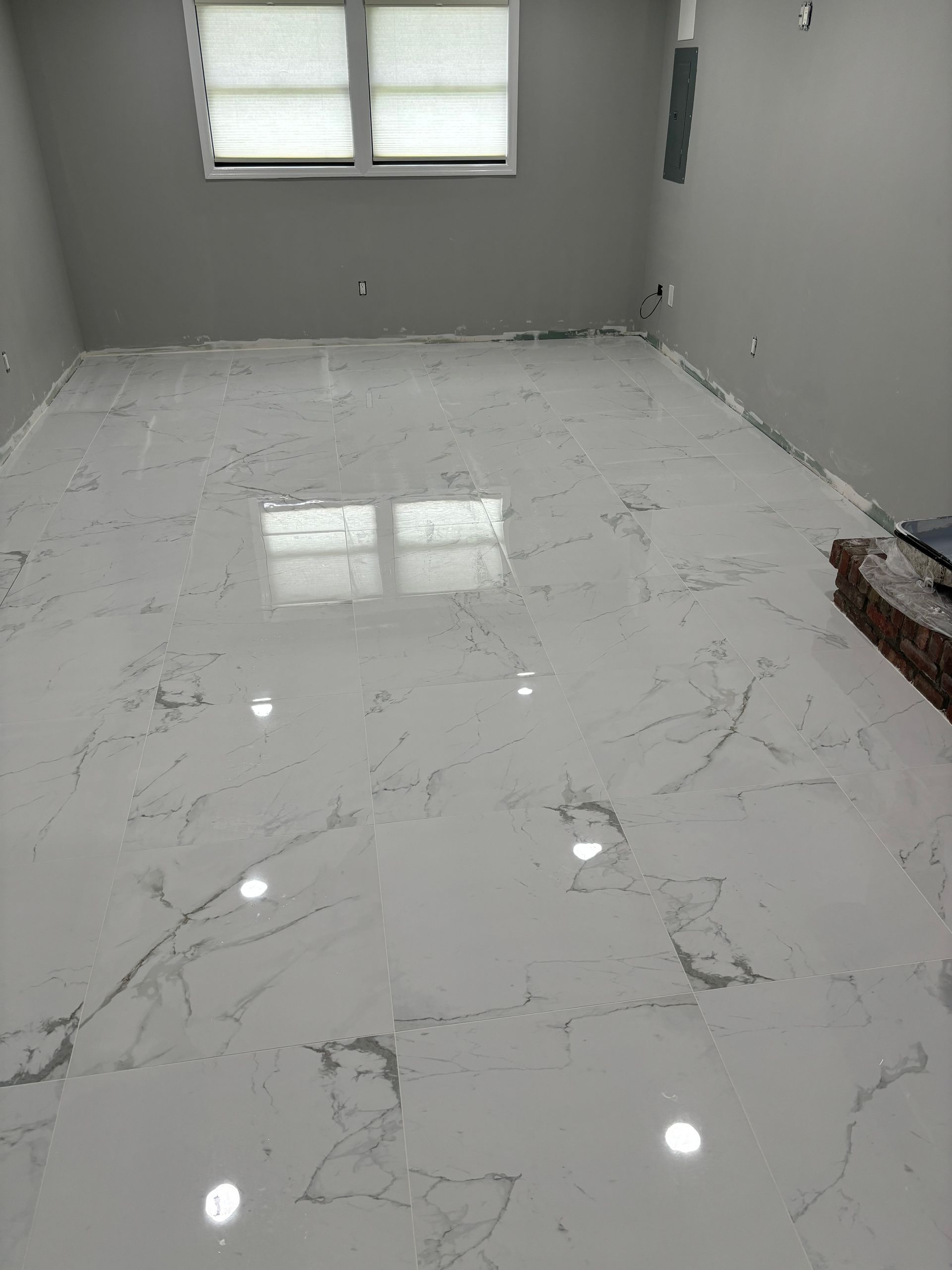 Room with newly installed white marble-look flooring reflecting light. Window in background.